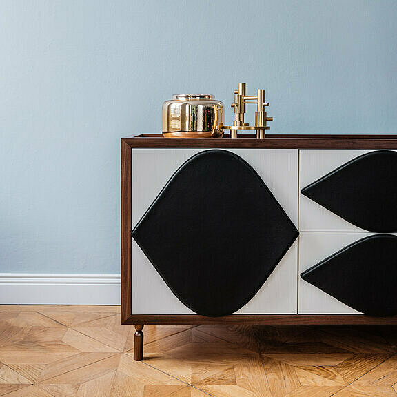 Antigua dresser with a white front and black leather handles against light blue wall