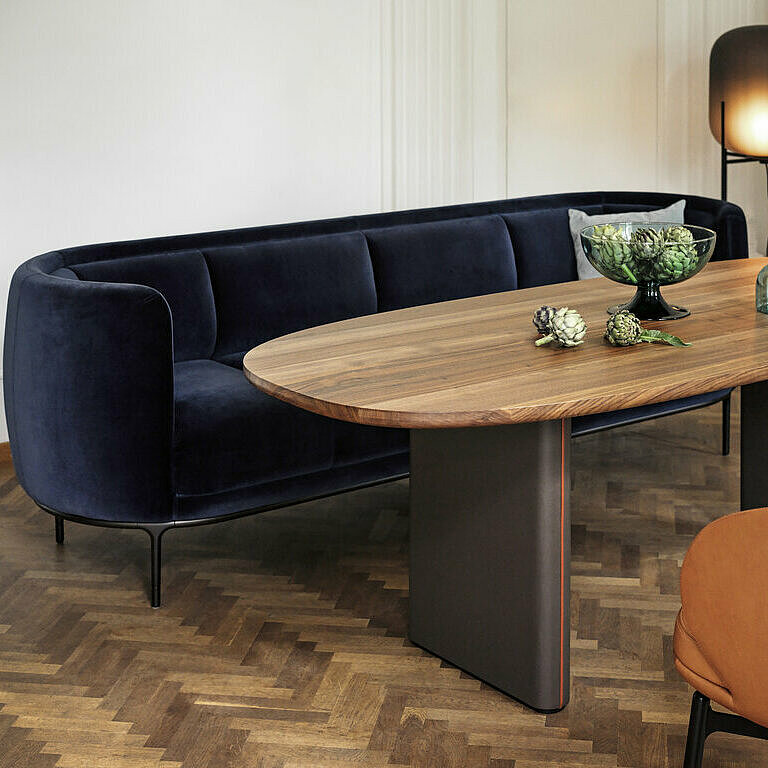 Vuelta sofa with dark blue velvet cover in front of Merwyn FD table with wooden top and Vuelta FD chair with cognac leather cover