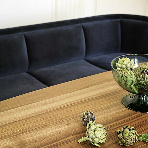 Vuelta Sofa mit dunkelblauem Samtbezug vor Tisch mit Holzplatte