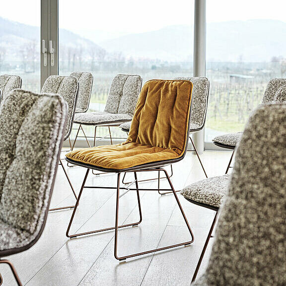 Aufstellung von Shilo Stühlen mit Salz/Pfeffer gemusterten Auflage, dazwischen ein Stuhl mit goldfarbener Auflage