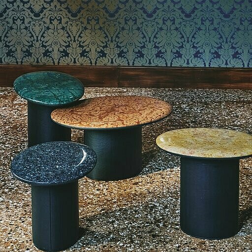 Vier ovale Beistelltische mit unterschiedlichen Marmorplatten auf Terrazzoboden vor Seidentapete