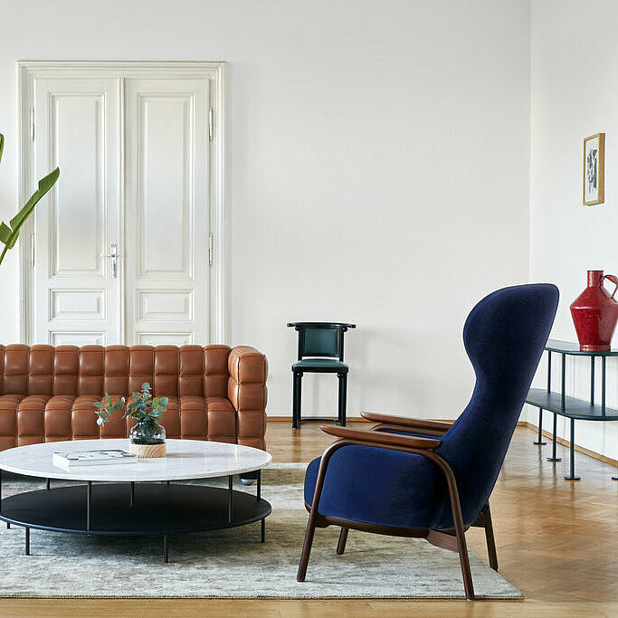 Vuelta high back chair covered with dark blue velvet in front of cognac leather cube sofa and DD-Table side table with marble top