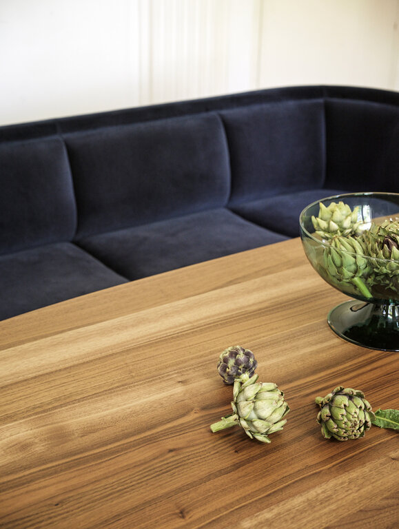 Vuelta Sofa mit dunkelblauem Samtbezug vor Tisch mit Holzplatte