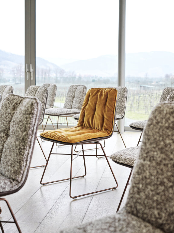 Aufstellung von Shilo Stühlen mit Salz/Pfeffer gemusterten Auflage, dazwischen ein Stuhl mit goldfarbener Auflage