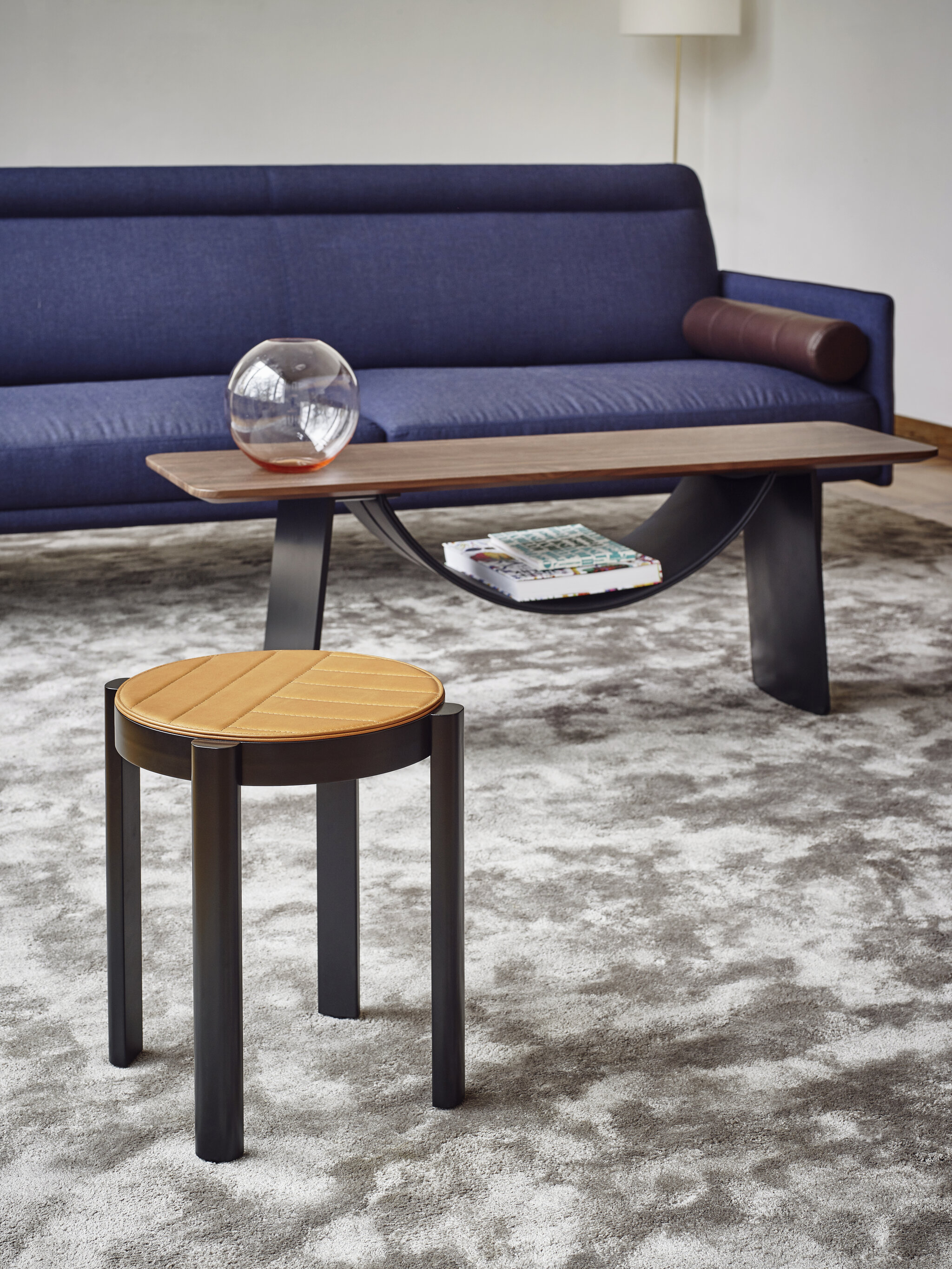 Melange Stool Table mit einer braunen gesteppten Lederplatte und schwarzen Fußgestell, dahinter zusehen ist der Melange Bridge Table und das Melange Sofa 